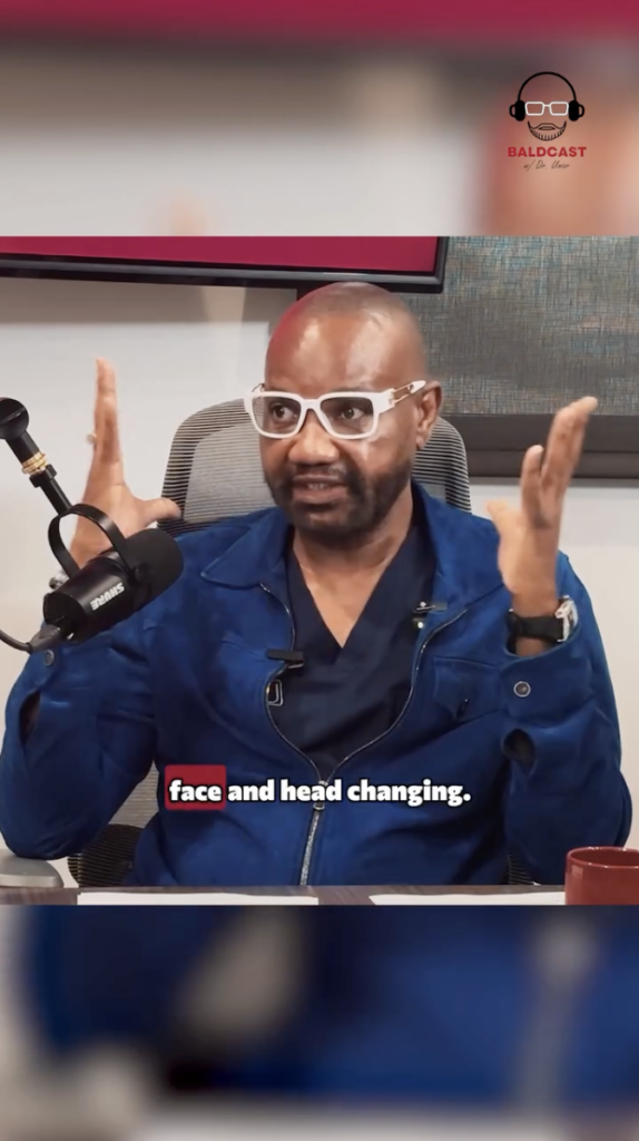 Dr. Sanusi Umar wearing white glasses and a blue jacket while speaking at a microphone.