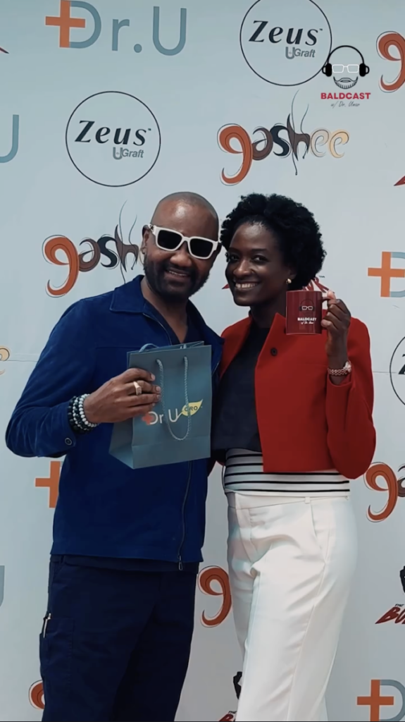 A man in white sunglasses and a woman in a red jacket standing together in front of a Dr. U and Zeus U Graft backdrop.