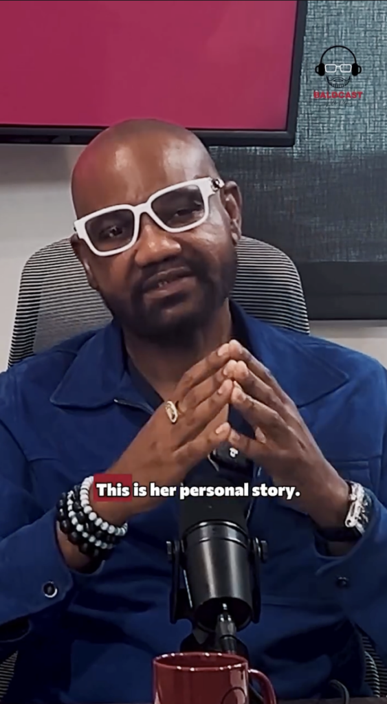 Bald man wearing white glasses and a blue jacket speaking into a microphone in a Baldcast studio.