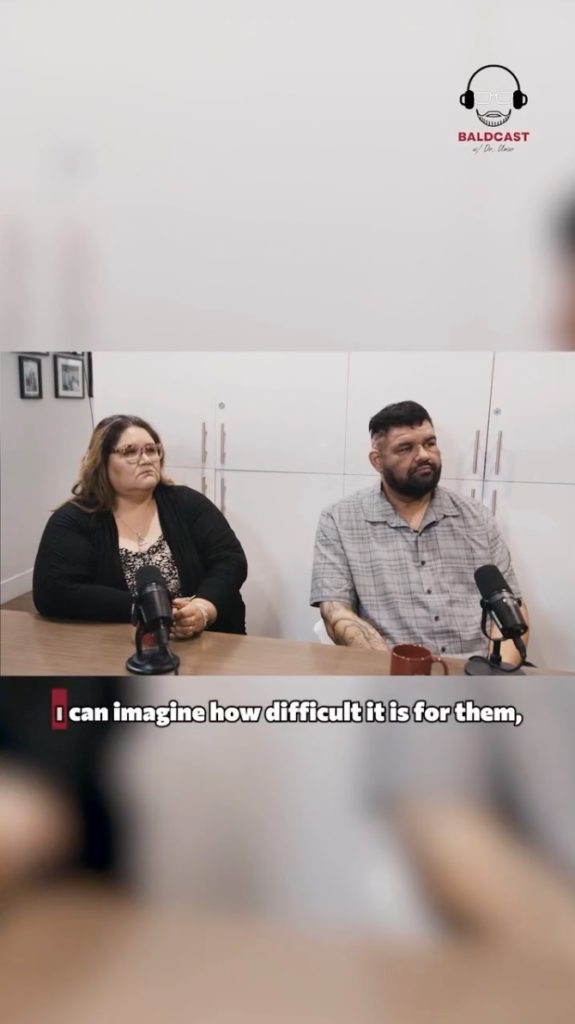 Two adults seated at a table with microphones during a Baldcast interview.