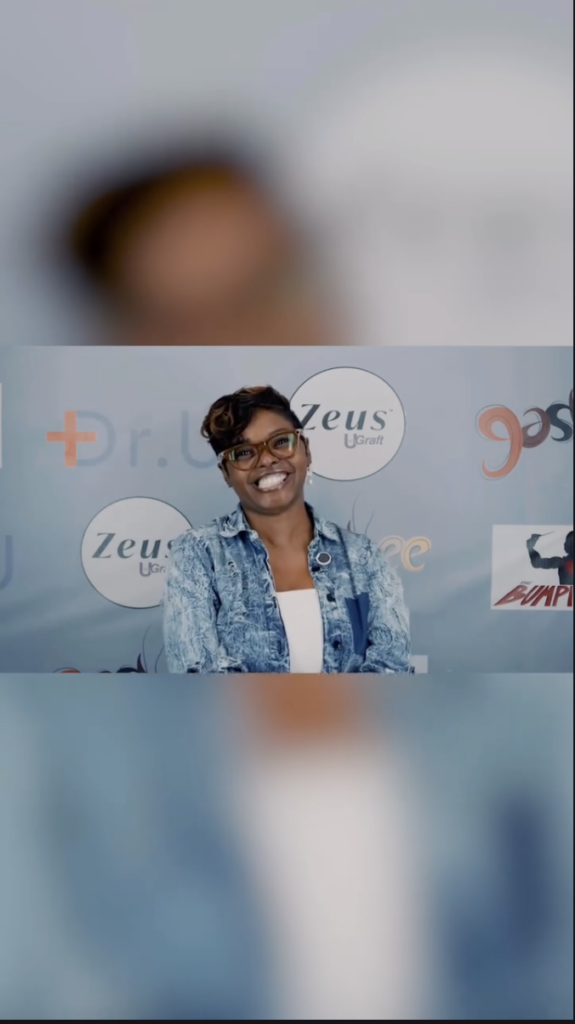 A woman wearing glasses and a blue patterned denim jacket smiling in front of a backdrop with Zeus and Bumpinator logos.