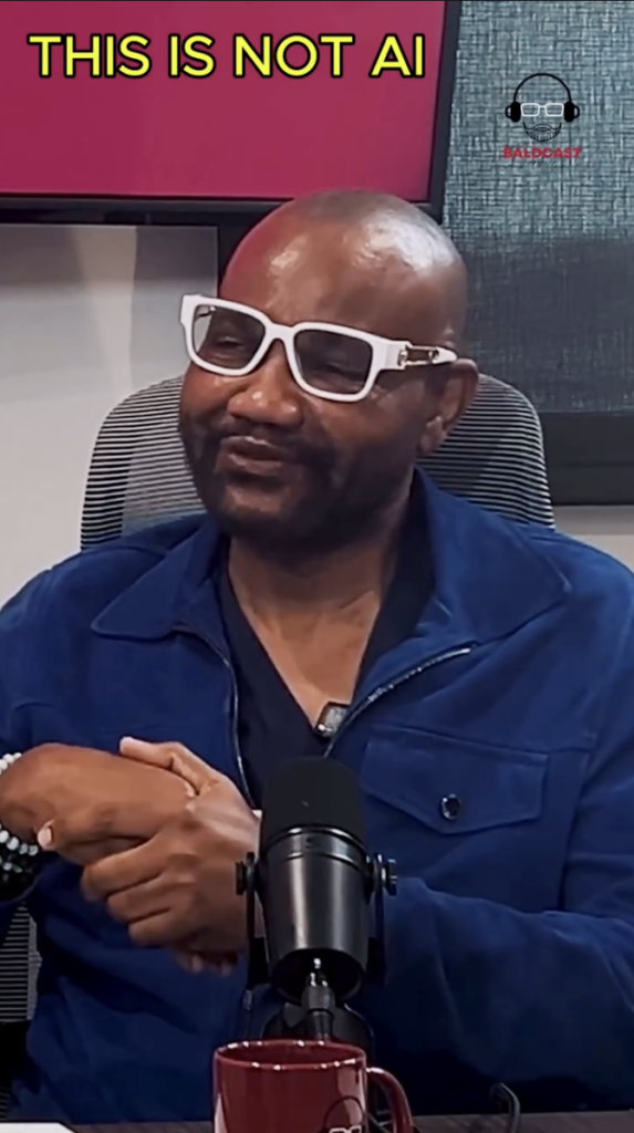 Man in white-framed glasses and blue jacket seated behind a tabletop microphone.
