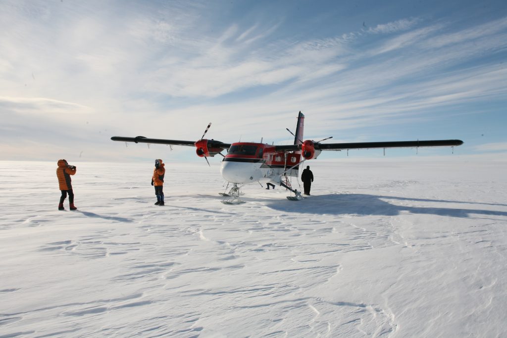 Expedition team at the start of a ski journey from Hercules Inlet, Antarctica, with an aircraft in the background.