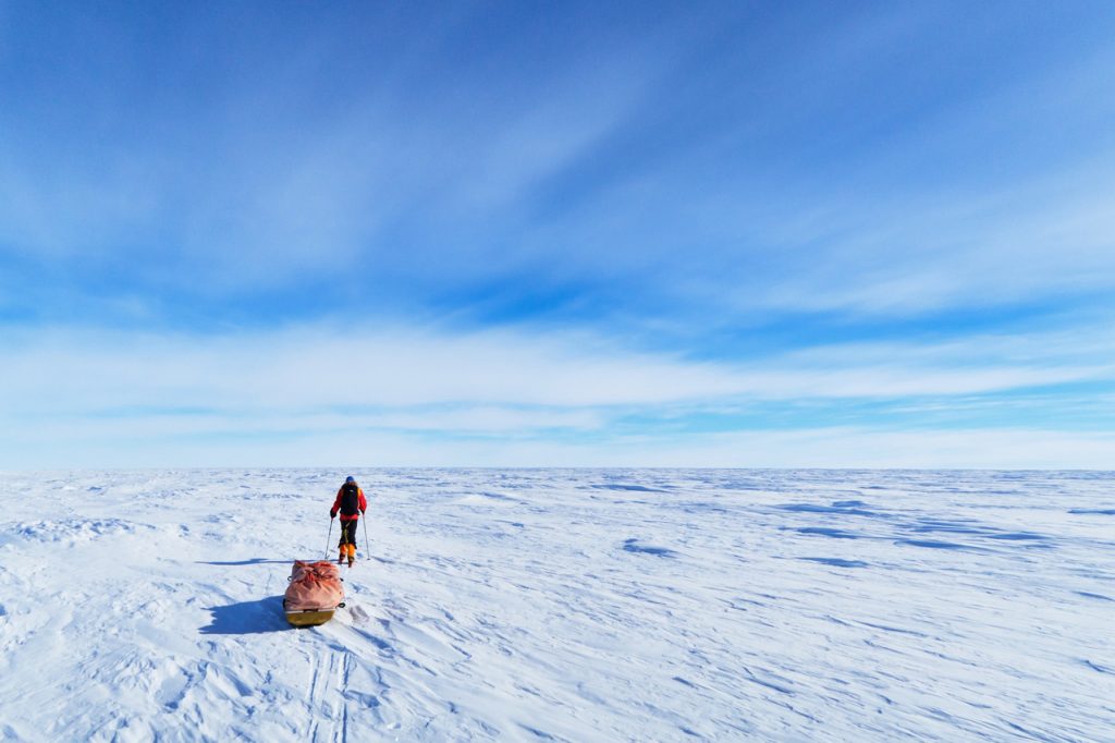 Skier pulling a sled across the snowy Antarctic polar plateau.