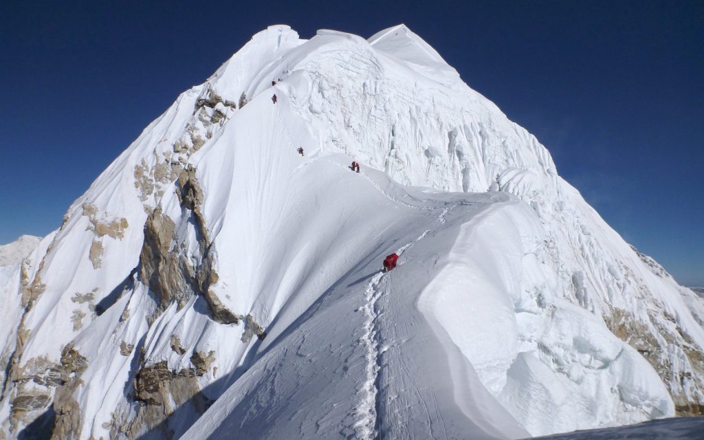 Climbers follow a trail up te snowy ridge of Baruntse in a clear day. 