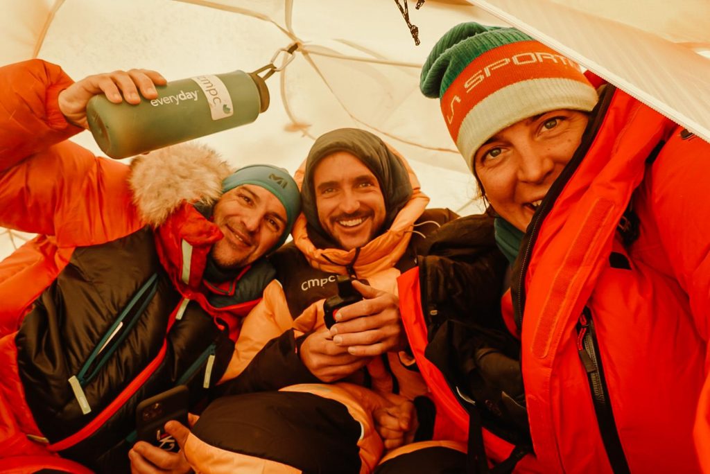 Climbers inside a small tent, smiling. 