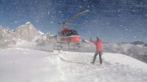 A helicopter lands on snow, a climber marks the spot.