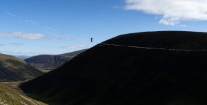 A person walks a highline rope suspended far above a Scottish valley.