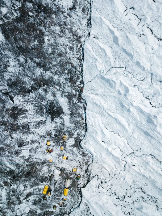 Aerial shot of tiny yellow tents on the huge Khumbu glacier, half of it partially rocky and half covered in ice and snow