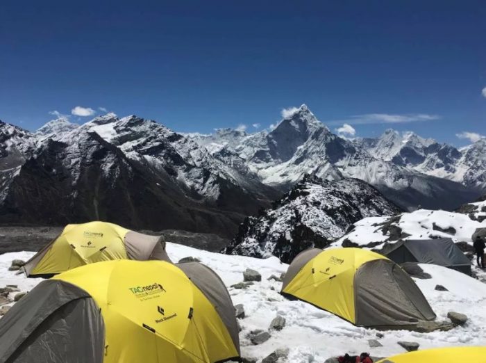 tents on a snow-rocky terrain at a plateau, imposing peaks in background. 