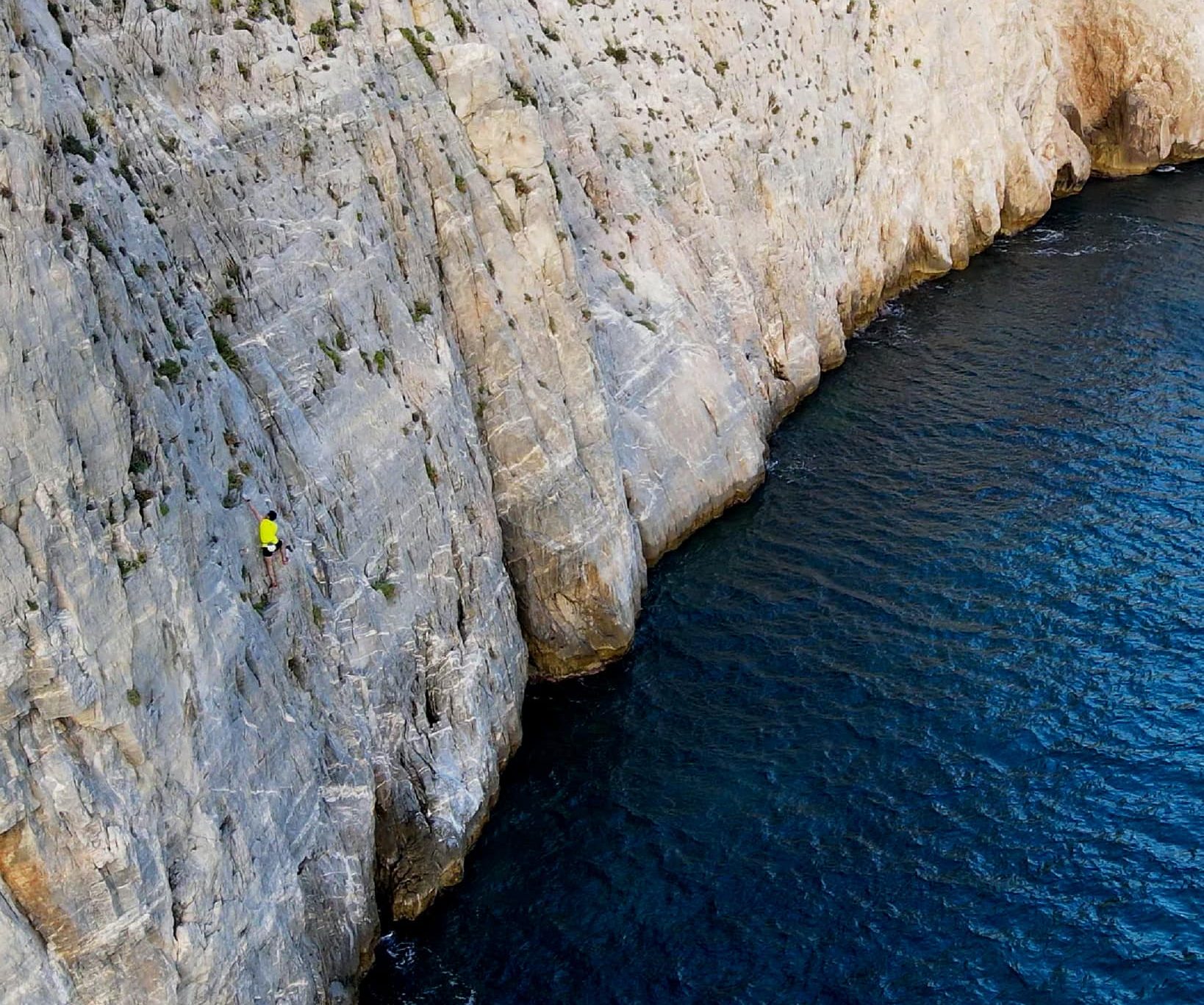 climber traversing a cliff, some 10 metres above the deep blue Mediterranean sea.