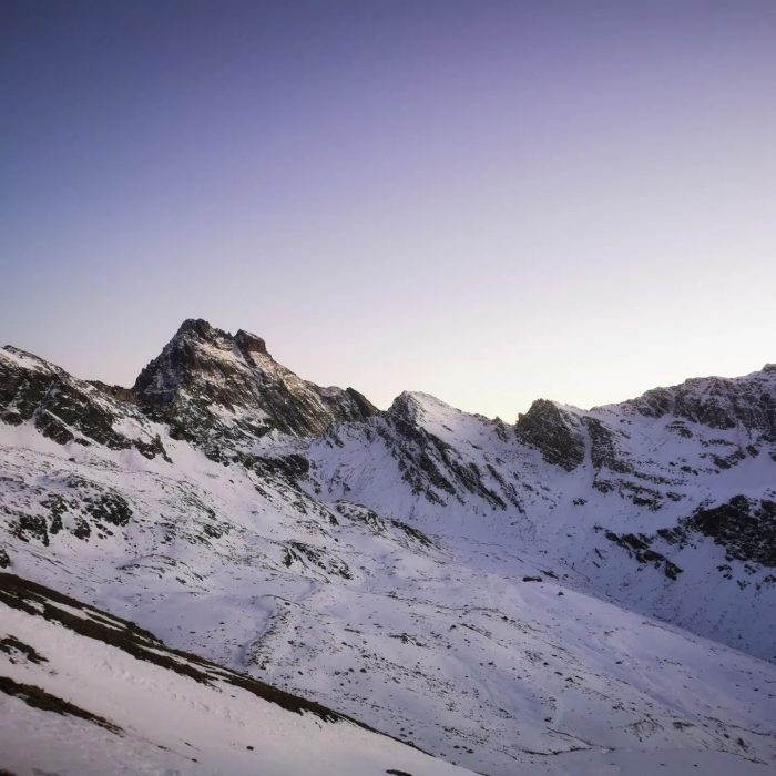 A rocky summmit rising on a ridge, with a thin layer of snow covering its flanks. 