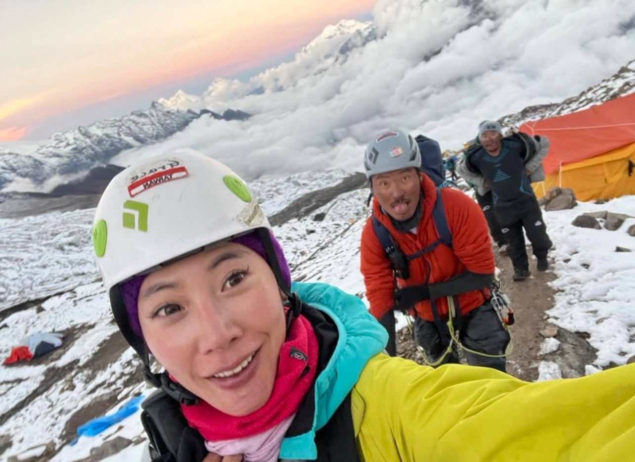 Selfie with sherpas behind her and clouds covering the valley in background.