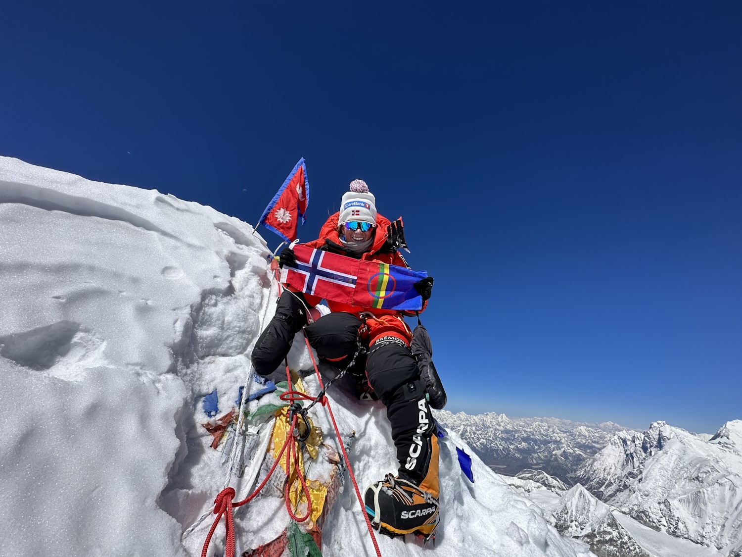 Harila poses on Makalu's sharp summit holding a Norwegian flag.