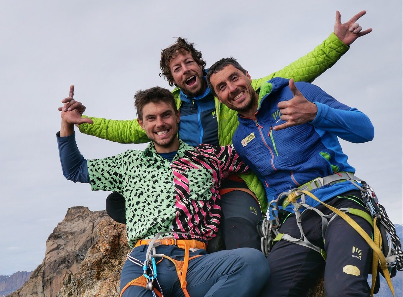 The climbers on rock climbing gear raise their arms on a summit.