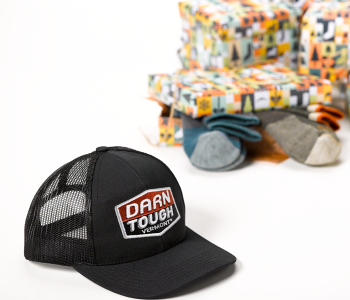 Our gorgeous Darn Tough Vermont Trucker hat, hanging out with some socks and holiday wrapping paper on a white background.
