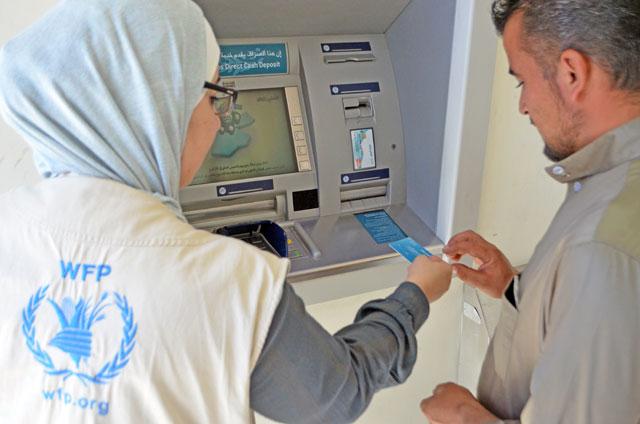 A member of the World Food Programme team assists a Syrian refugee in using the blockchain method in Azraq refugee camp A member of the World Food Programme team assists a Syrian refugee in using the blockchain method in Azraq refugee camp