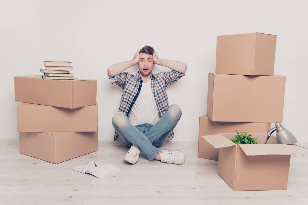 boy sitting on ground with hands on head looking overwhelmed next to moving boxes