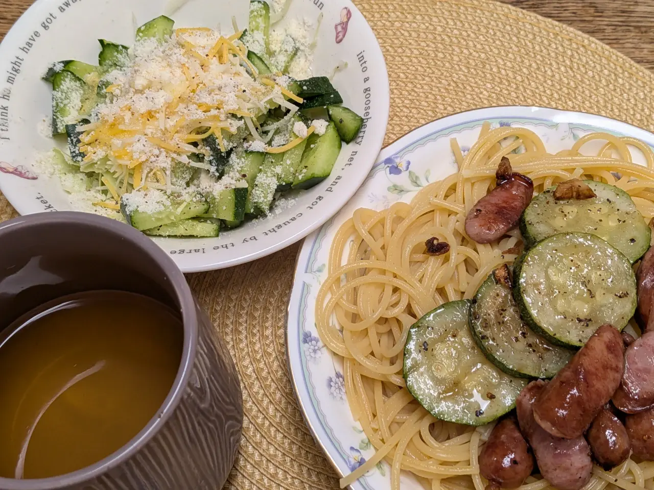 ズッキーニとソーセージ炒めのスパゲッティ、チーズ乗せサラダ、リンゴジュースの入ったコップの写真