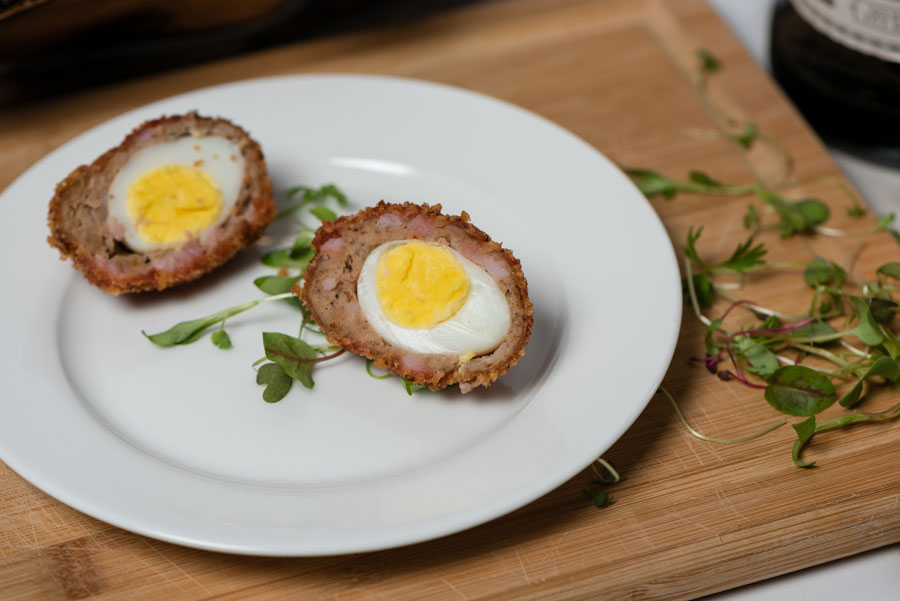 Two scotch eggs on a white plate.
