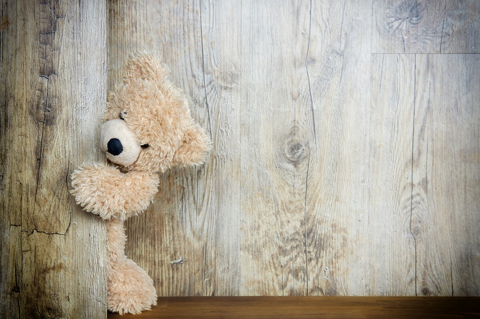 A beige teddy bear peaks around a corner.