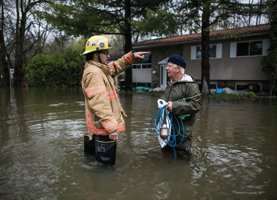 An older man speaking with an emergency relief worker in knee hight flood waters.