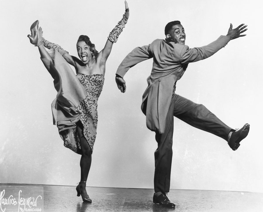 Two dancers kicking their legs out in opposite directions.