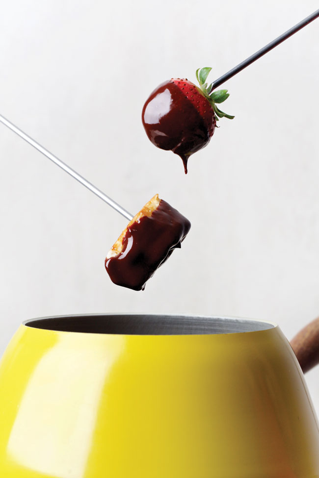 A skewer holding a strawberry dripping in chocolate emerging from a fondue pot.