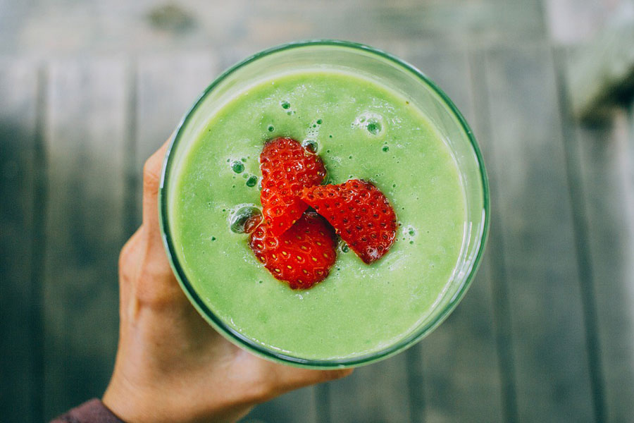 The above view of a green smoothie with slices of strawberry floating on top.