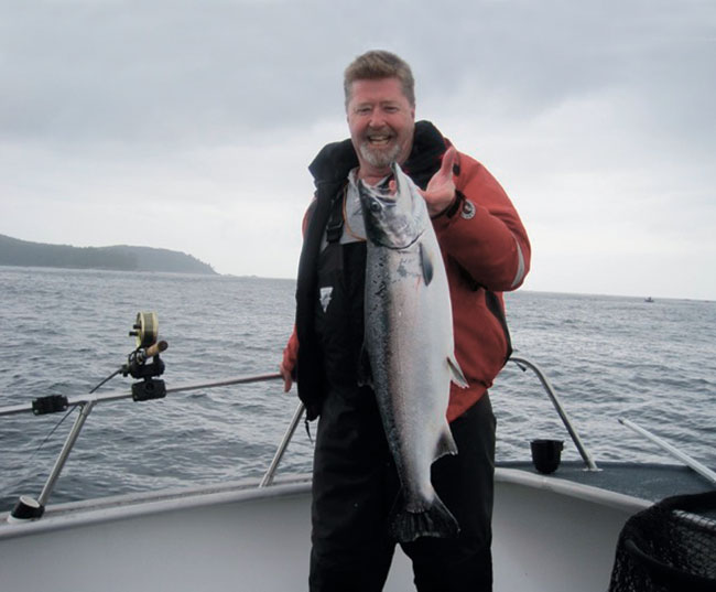 A man smiling as he holds a fish that he caught by the hook.