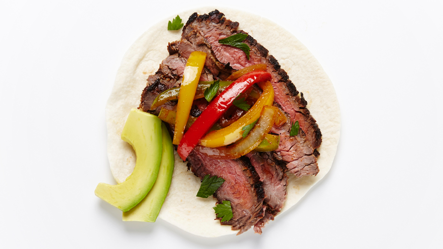Grilled flank steak on a fajita with red and yellow peppers and avocado.