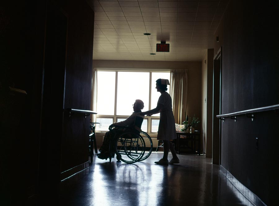 A nurse pushing a woman in a wheelchair in a nursing home.