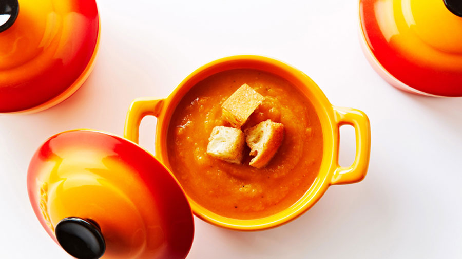 Butter nut squash and sweet potato soup in an orange cup.