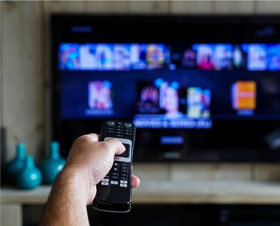 A hand holding a remote pointed toward a TV.