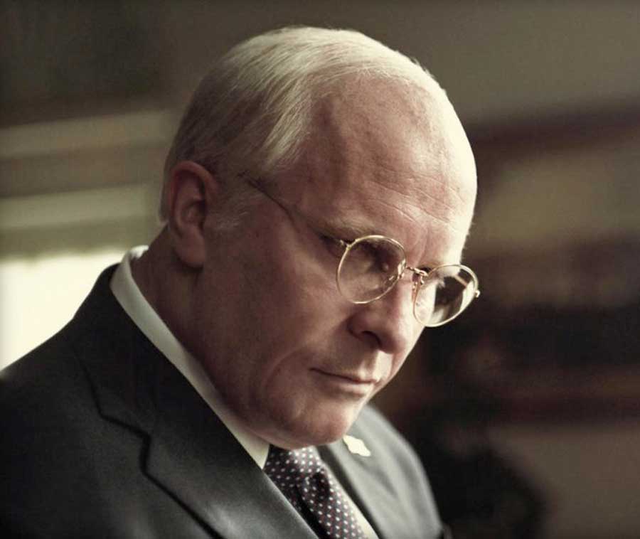 Christian Bale&#039;s as Dick Cheney glances down wearing a pari of glasses and a suit.