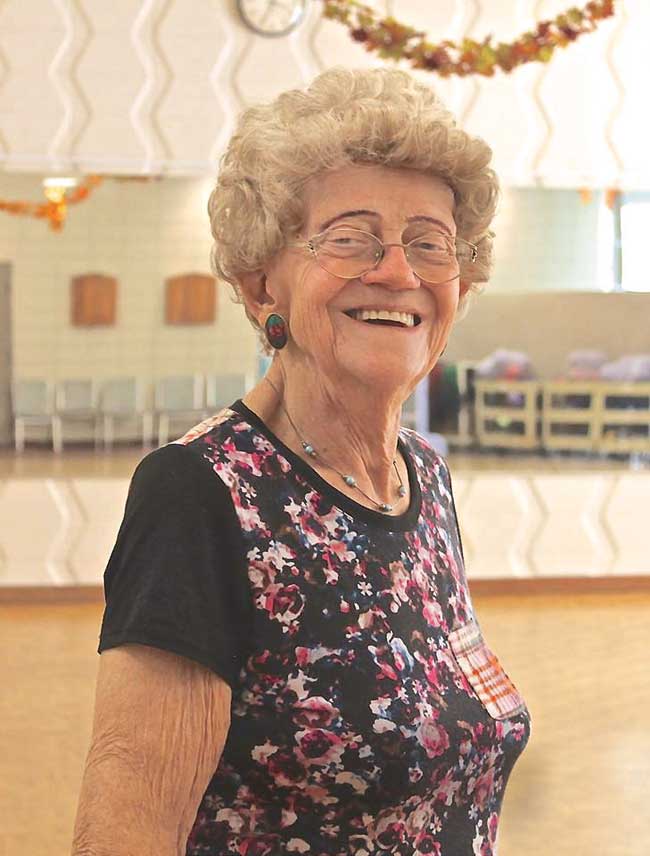 A woman with a short perm wearing a floral shirt, smiling.