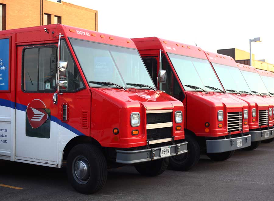 A line of Canada post trucks in a parking lot.