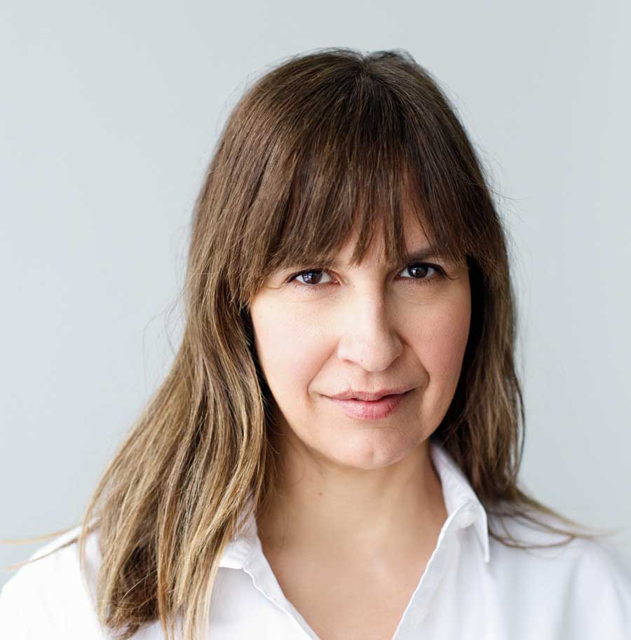 A portrait of Canadian Author Lisa Gabriele, bangs partially over her eyebrows, wearing a white dress shirt with the top button undone.