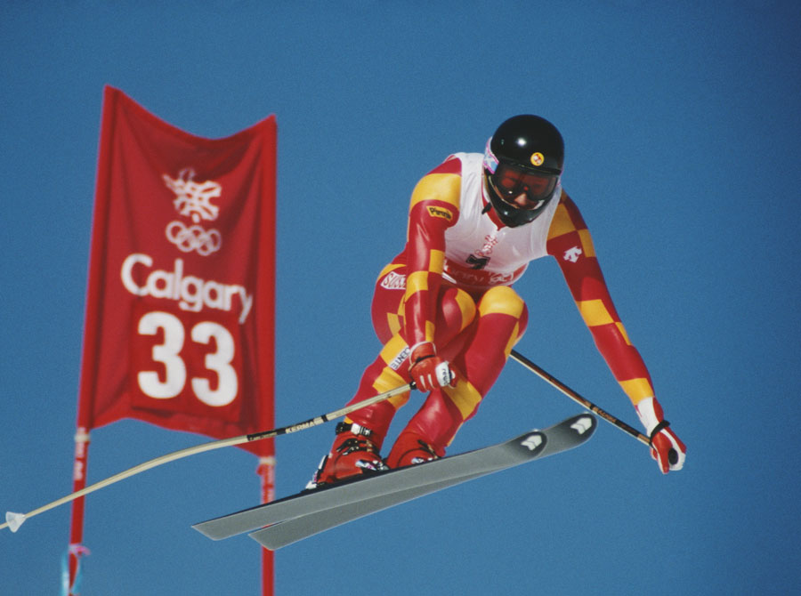 A skier in mid-air beside a promotional sign for the Calgary Olympics.