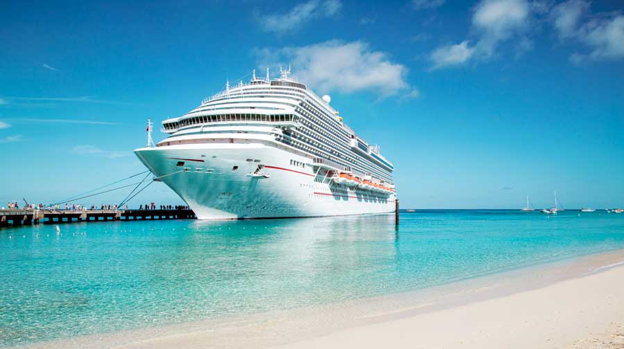 A cruise ship near the shore on a caribbean beach with white sand and bright blue water.