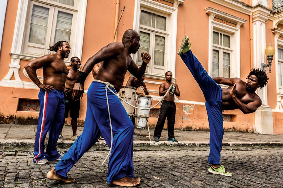 Two men practicing martial arts, one crouched and kicking at head level.