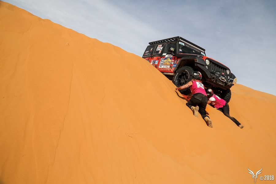 A jeep stuck on a sand dune in the Sahara Desert as two competitors attempt to dig it out.