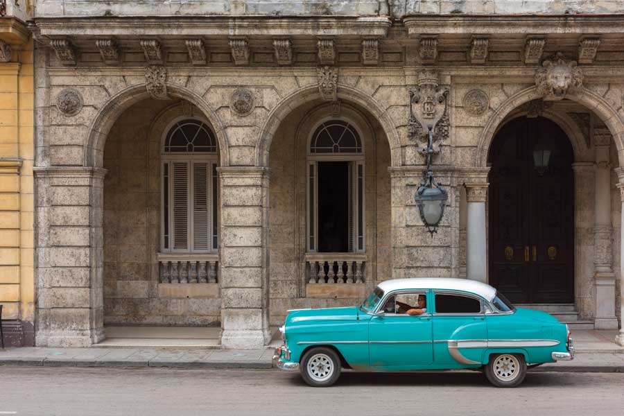 A turquoise 1960s style car sitting in front of an old building in Old Havana.