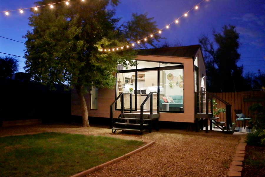 A tiny house with a large glass front window that the kitchen can be seen through.