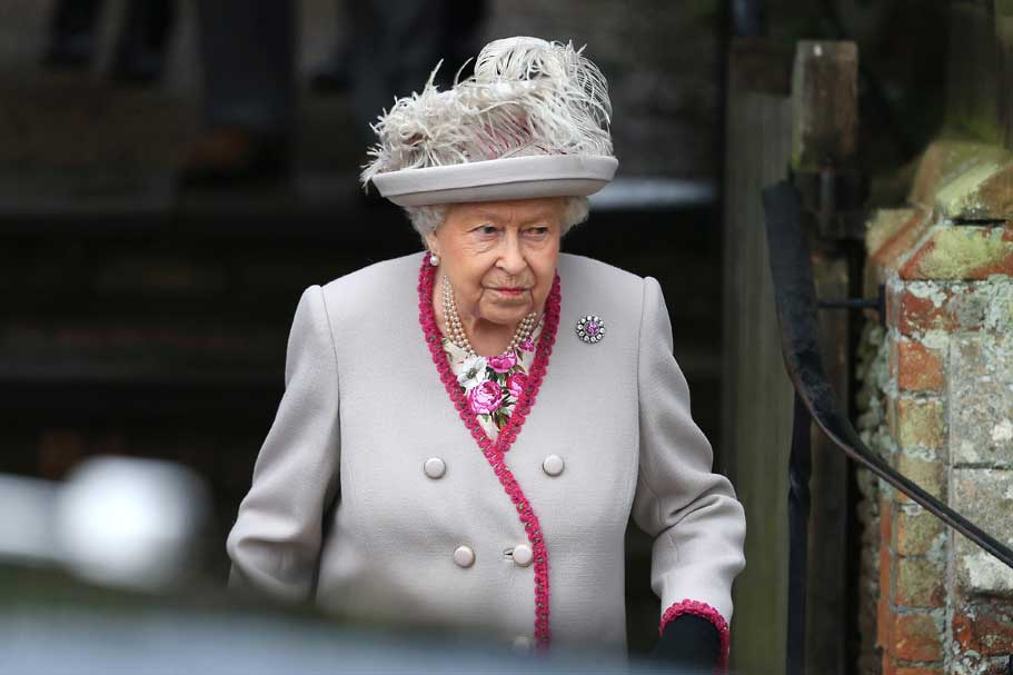 Queen Elizabeth wearing a grey suit and feathered hat.