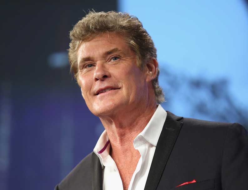 David Hasselhoff smiling, wearing a black suit jacket and a white sure with top two buttons open.