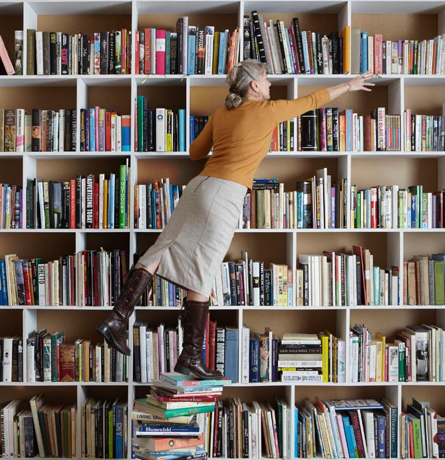 Time to de-clutter. Woman standing on stack of books.