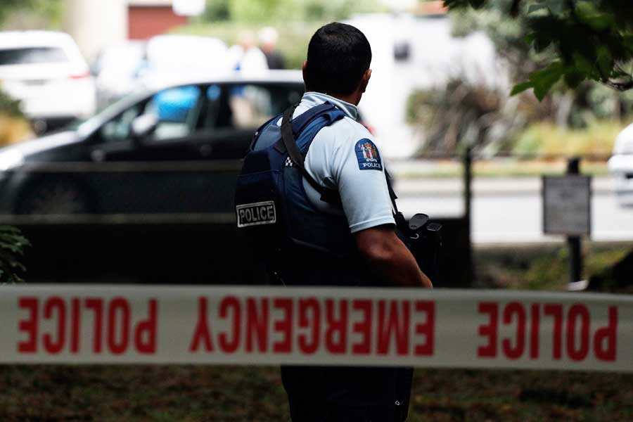 A police officer standing with his back turned behind police tape.