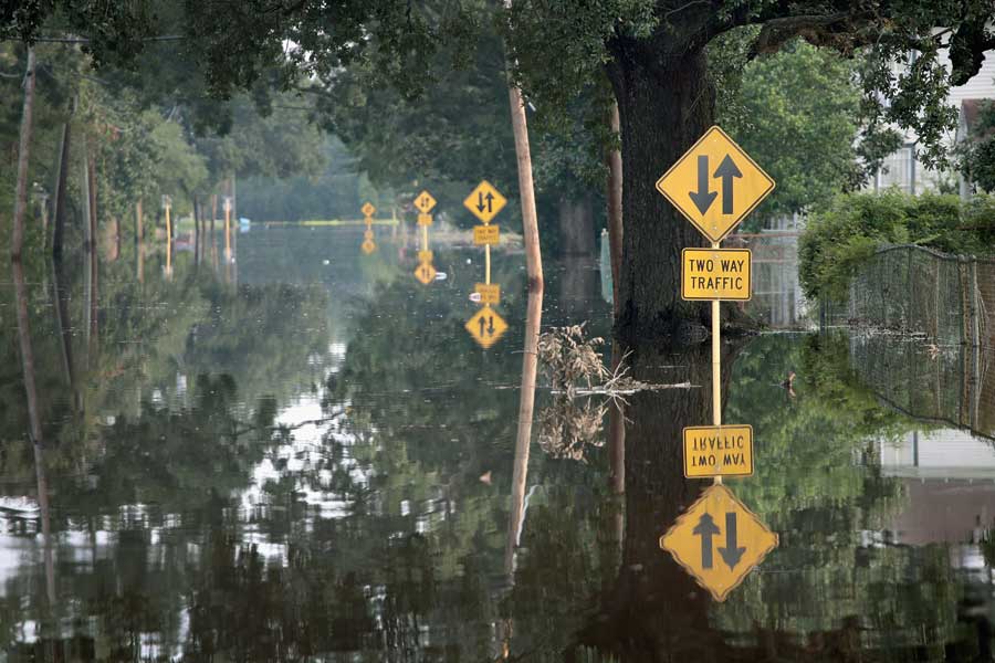 A flooded road with two way traffic signs sticking out from the lake of water.