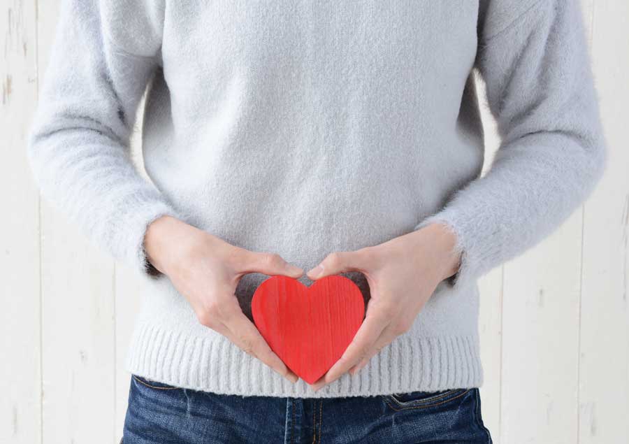 A person holding a red heart close to their stomach.